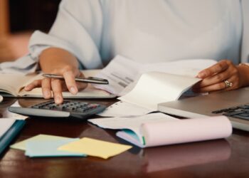 Pessoa à mesa fazendo contas com calculadora, caneta e boletos ao lado do notebook, cena que representa o passo a passo para renegociar dívidas no Novo Desenrola Brasil.