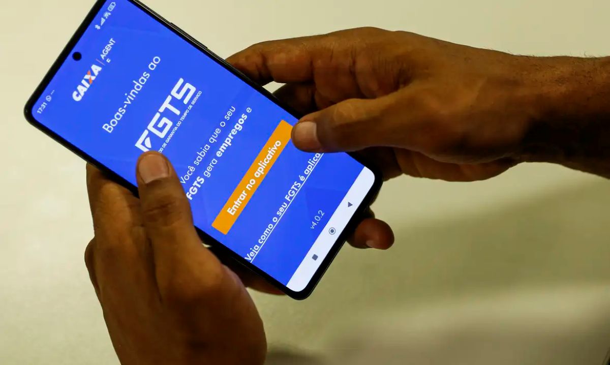Mãos seguram um celular aberto no aplicativo FGTS da Caixa, na tela de boas-vindas