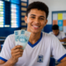 Estudante de uniforme sorri segurando duas cédulas de cem reais em uma sala de aula