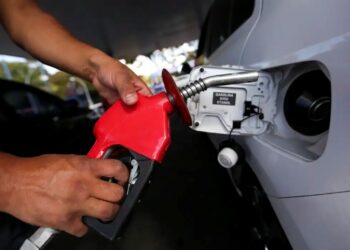 Pessoa segura bomba de combustível vermelha enquanto abastece carro em posto de gasolina