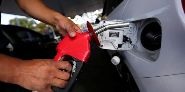 Pessoa segura bomba de combustível vermelha enquanto abastece carro em posto de gasolina