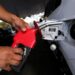 Pessoa segura bomba de combustível vermelha enquanto abastece carro em posto de gasolina