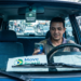 Motorista de aplicativo usa o celular dentro do carro, com cartaz do programa Move Brasil no painel.