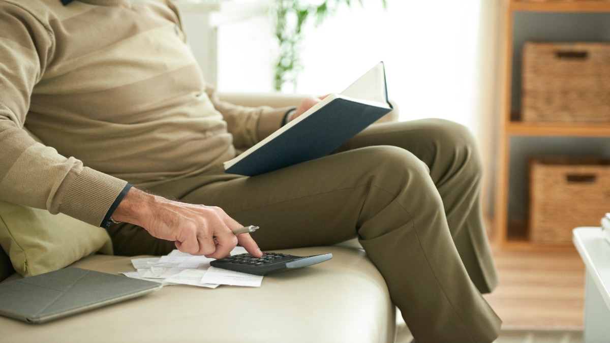 Homem sentado no sofá conferindo contas em papéis com uma calculadora e um caderno, cena que representa a renegociação de dívidas pelo Novo Desenrola Brasil.
