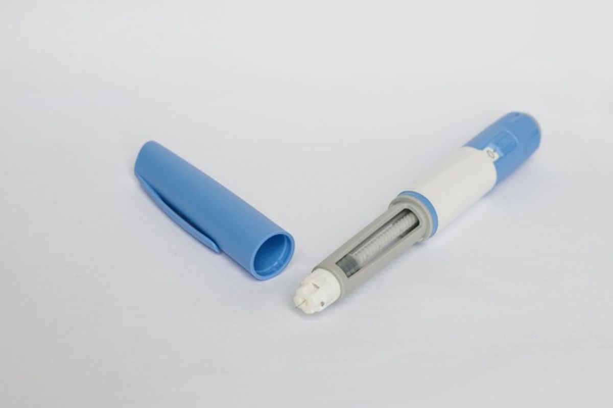 Caneta de aplicação de medicamento injetável azul e branca, com a tampa ao lado, sobre fundo claro