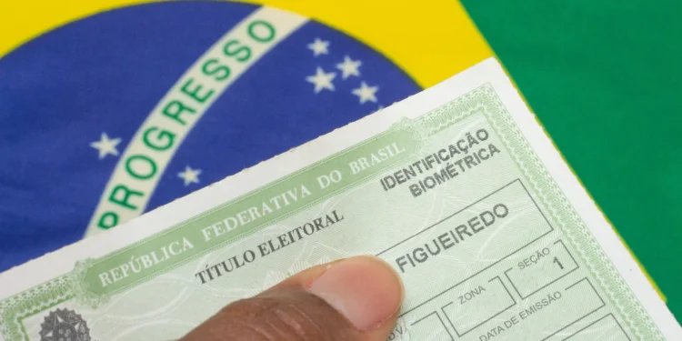 Mão segurando título eleitoral do Brasil com campo de biometria sobre bandeira verde e amarela.