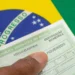 Mão segurando título eleitoral do Brasil com campo de biometria sobre bandeira verde e amarela.