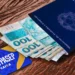 Carteira de Trabalho azul aberta com várias notas de 100 reais saindo de dentro. Ao lado, um cartão azul e amarelo com a inscrição "PIS/PASEP CAIXA". A imagem está sobre uma superfície de madeira.