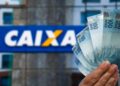 Mão segura cédulas de cem reais diante de fachada da Caixa Econômica Federal, em referência ao saque de até R$ 6.220
