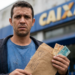 Homem segura um envelope com cédulas de dinheiro em frente a uma agência da Caixa