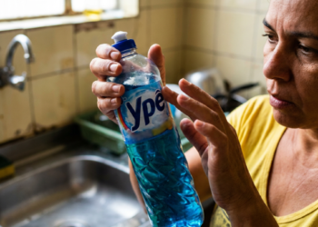 Mulher observa atentamente um frasco de detergente da marca Ypê