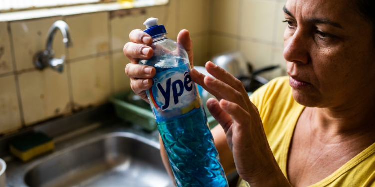 Mulher observa atentamente um frasco de detergente da marca Ypê