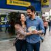 Casal feliz segura notas de reais ao sair da agência do Banco do Brasil no centro urbano