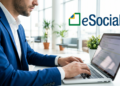 Empresário digitando em laptop com logo do eSocial em ambiente corporativo.