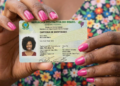 Mulher mostra carteira de identidade brasileira com unhas rosa e vestido floral.