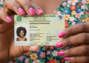 Mulher mostra carteira de identidade brasileira com unhas rosa e vestido floral.