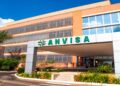 Fachada do prédio da Anvisa com letreiro verde sob céu azul e plantas ao redor