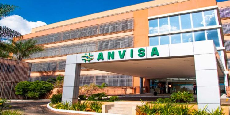 Fachada do prédio da Anvisa com letreiro verde sob céu azul e plantas ao redor