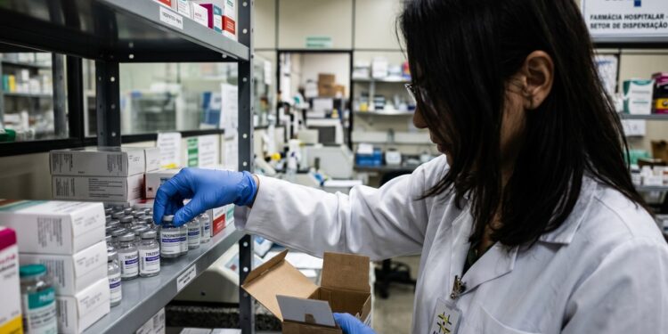 Agente técnica da Anvisa com jaleco branco inspeciona frascos de tirzepatida em prateleira de farmácia hospitalar vinculada ao SUS.