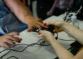 Mão de mulher sendo posicionada em leitor biométrico com manicure vermelha sobre mesa branca com computador
