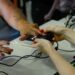 Mão de mulher sendo posicionada em leitor biométrico com manicure vermelha sobre mesa branca com computador