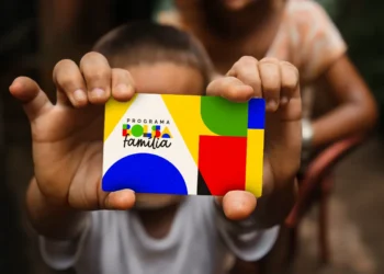 Mulher segurando cartão do Bolsa Família em destaque, ilustrando risco de bloqueio do benefício por pendências na área da saúde.