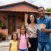 Família com quatro pessoas sorri segurando notas de real em frente à casa colorida