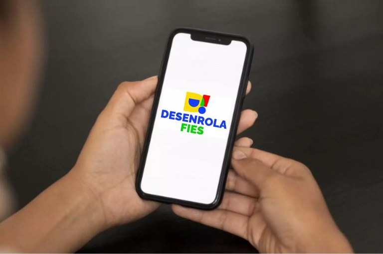 Mãos seguram celular com logo Desenrola Fies na tela; fundo escuro, foco em renegociação estudantil