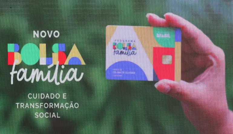 Mão segurando cartão colorido do novo Bolsa Família ao lado do slogan cuidado e transformação social