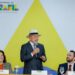 Presidente Lula, usando chapéu panamá, discursa ao microfone em evento do Governo do Brasil com painel colorido ao fundo