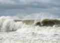 Ondas gigantes quebrando em mar agitado sob céu nublado.