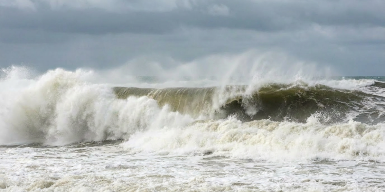 Ondas gigantes quebrando em mar agitado sob céu nublado.
