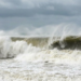 Ondas gigantes quebrando em mar agitado sob céu nublado.