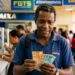 Homem segura notas de R$ 50 e R$ 100 em agência da Caixa com placas FGTS e Saque ao fundo