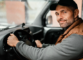 Motorista de boné sorrindo ao volante dentro de veículo utilitário.