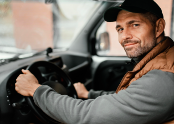 Motorista de boné sorrindo ao volante dentro de veículo utilitário.