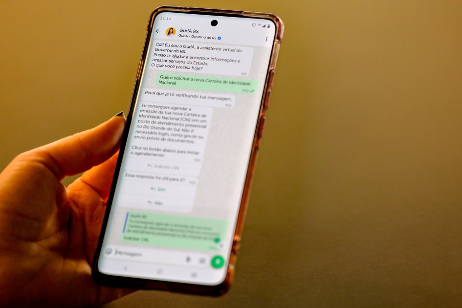 Mão segura celular exibindo conversa no WhatsApp com GurIA RS sobre solicitação de carteira de identidade
