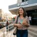 Mulher sorrindo segura notas de real ao sair do INSS, rampa acessível ao fundo