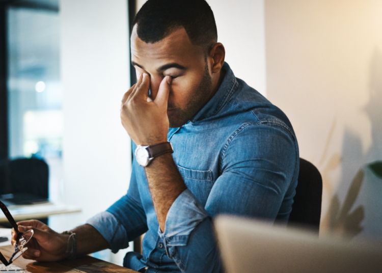 Profissional cansado esfrega os olhos em frente ao computador no escritório.