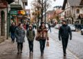 Grupo de quatro pessoas com roupas de frio caminha pelo centro de Gramado, com lojas e placas visíveis ao fundo