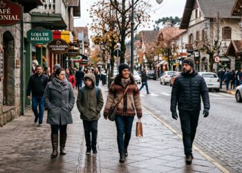 Grupo de quatro pessoas com roupas de frio caminha pelo centro de Gramado, com lojas e placas visíveis ao fundo