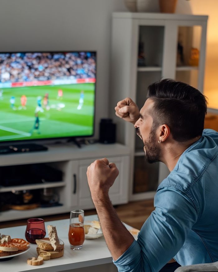 Homem assistindo jogo de futebol na televisão.