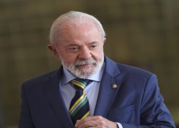Lula com terno azul e gravata verde-amarela em ambiente oficial, sorrindo discretamente
