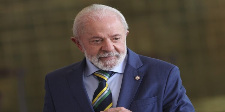 Lula com terno azul e gravata verde-amarela em ambiente oficial, sorrindo discretamente