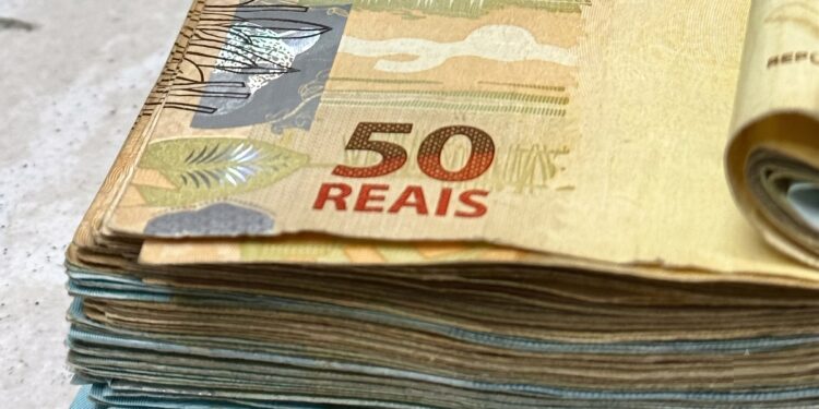 Maço de notas de cinquenta reais em destaque sobre superfície clara