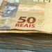 Maço de notas de cinquenta reais em destaque sobre superfície clara