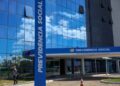 Fachada espelhada do prédio do INSS Previdência Social com céu azul refletido e mulher caminhando