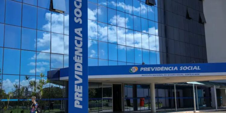 Fachada espelhada do prédio do INSS Previdência Social com céu azul refletido e mulher caminhando