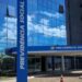 Fachada espelhada do prédio do INSS Previdência Social com céu azul refletido e mulher caminhando
