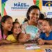Mulher sorridente mostra notas de 100 reais junto a três crianças em evento do Mães de Pernambuco